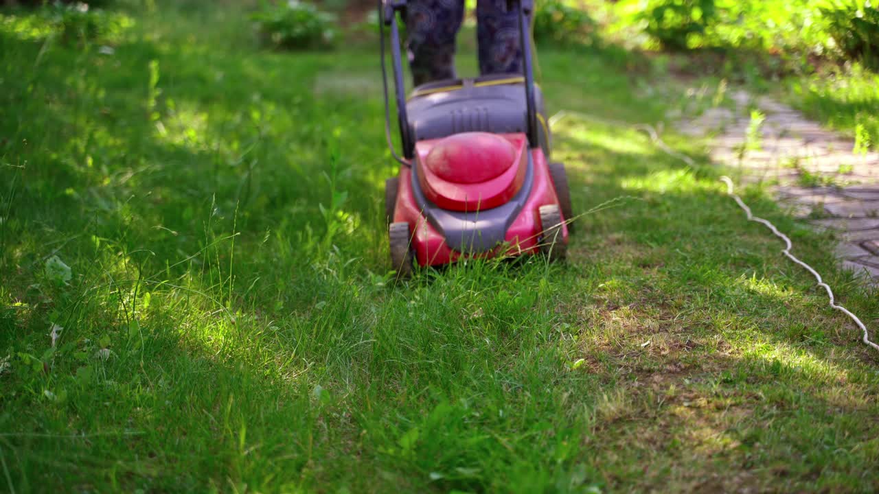 Grass mower in the yard. Electric lawn mower at motion. Worker cutting grass in the garden. Gardening concept.
