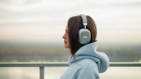 close-up side view of woman in hoodie and headphones walking gently, blinking eyes, peaceful walk by river, calm outdoor setting with blurred river view in background, tranquil atmosphere
