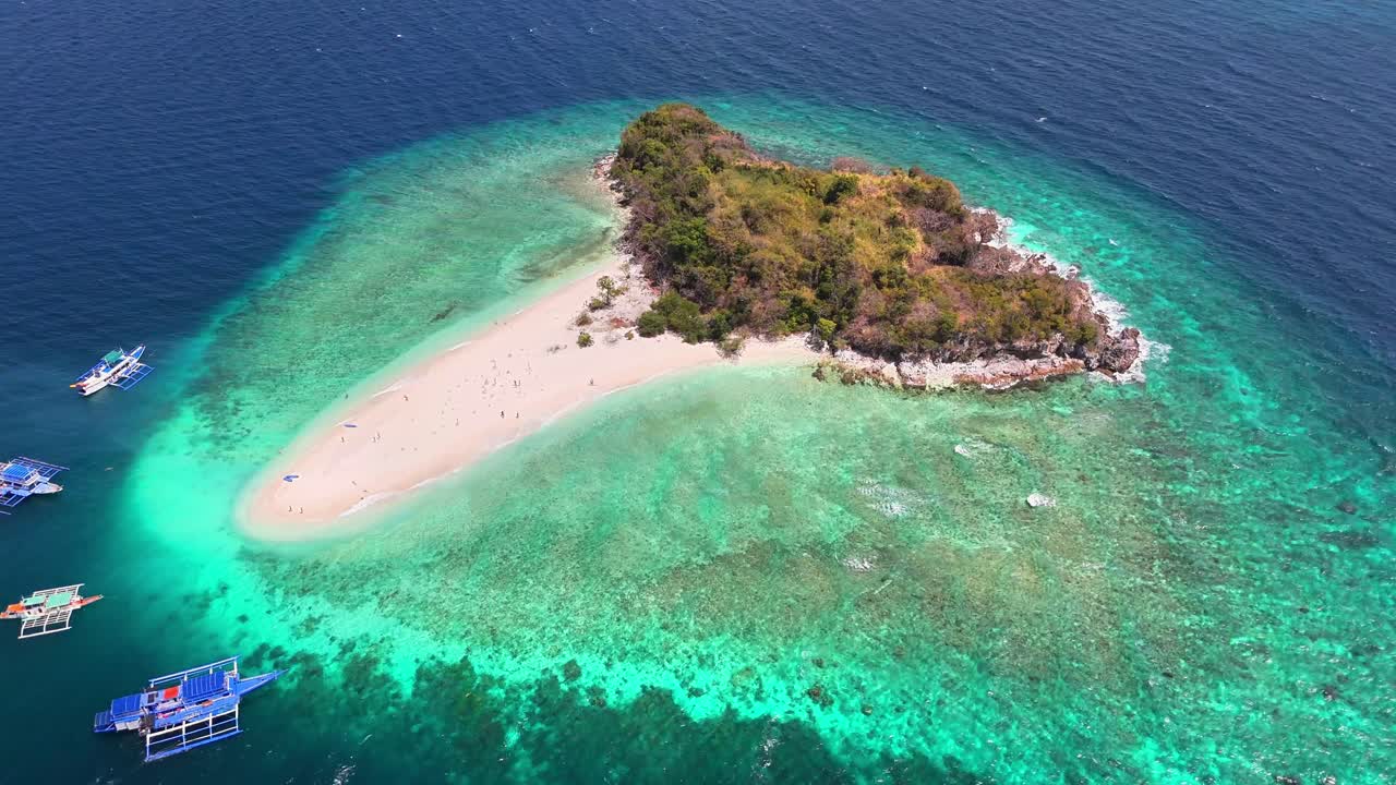Aerial view of Tacling Island in Linapacan, Philippines with vibrant coral reefs, turquoise waters, and traditional boats near a white sand beach surrounded by lush greenery and deep blue ocean