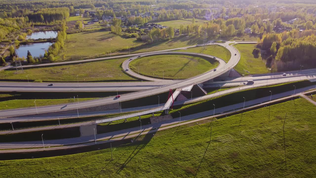 Multi level road system winds through Latvian suburb with traffic and greenery, aerial medium establishing