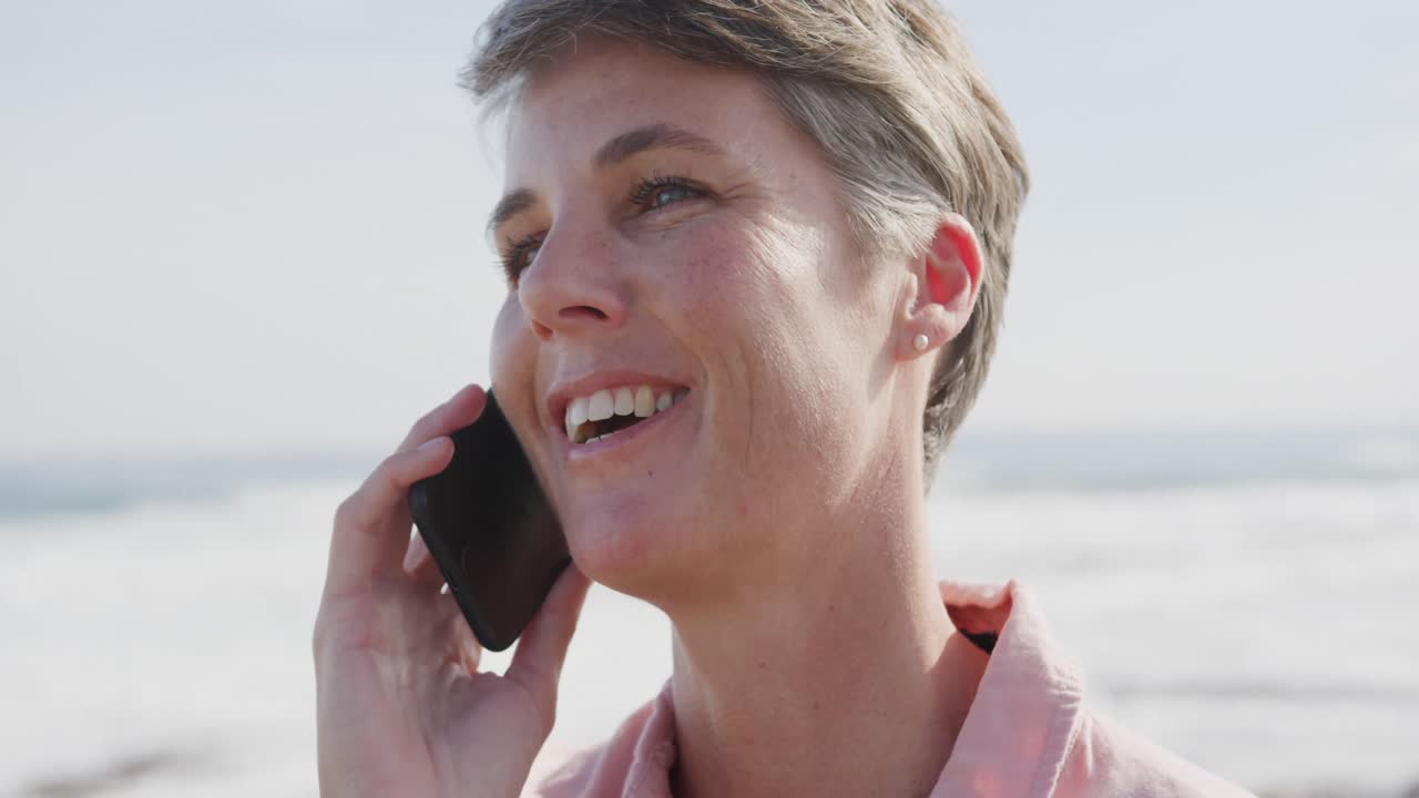 Caucasian woman enjoying free time by sea on sunny day talking on phone