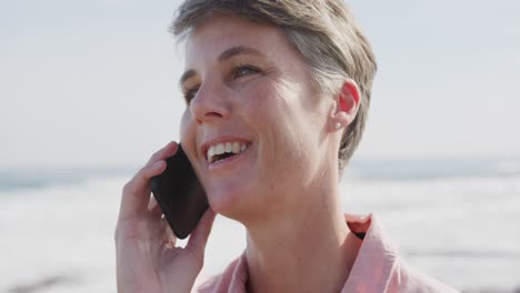 Caucasian-woman-enjoying-free-time-by-sea-on-sunny-day-talking-on-phone