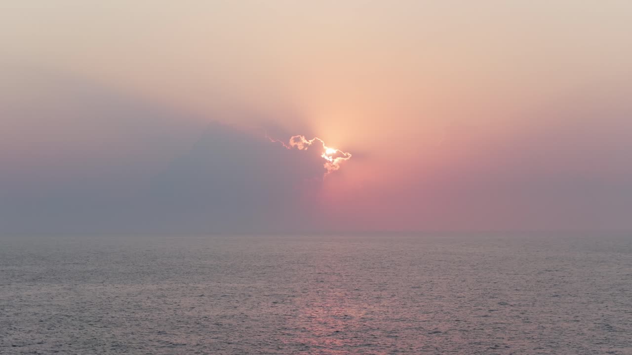 Sunrise over sea, sun shines through clouds, casting rays of light on calm water. Aerial drone, copy space