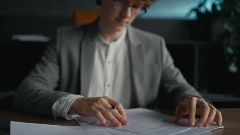 close-up a confident young guy with curly hair in a gray jacket examines documents and signs while sitting at a table in the office