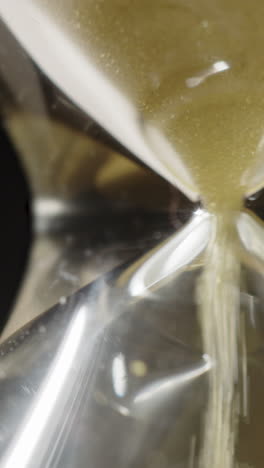 vertical extreme closeup of grains of yellow sand flowing through an hourglass