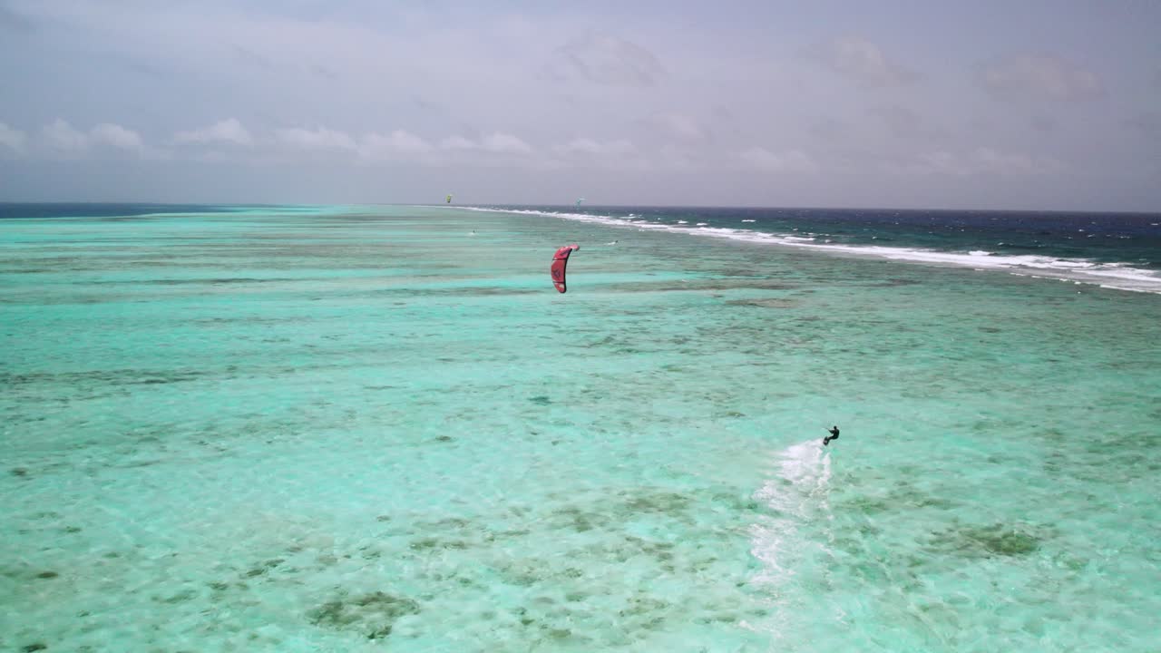 un kite surfer solitario deslizándose sobre las vibrantes aguas turquesas de los rocas con una barrera de arrecifes distante, vista aérea