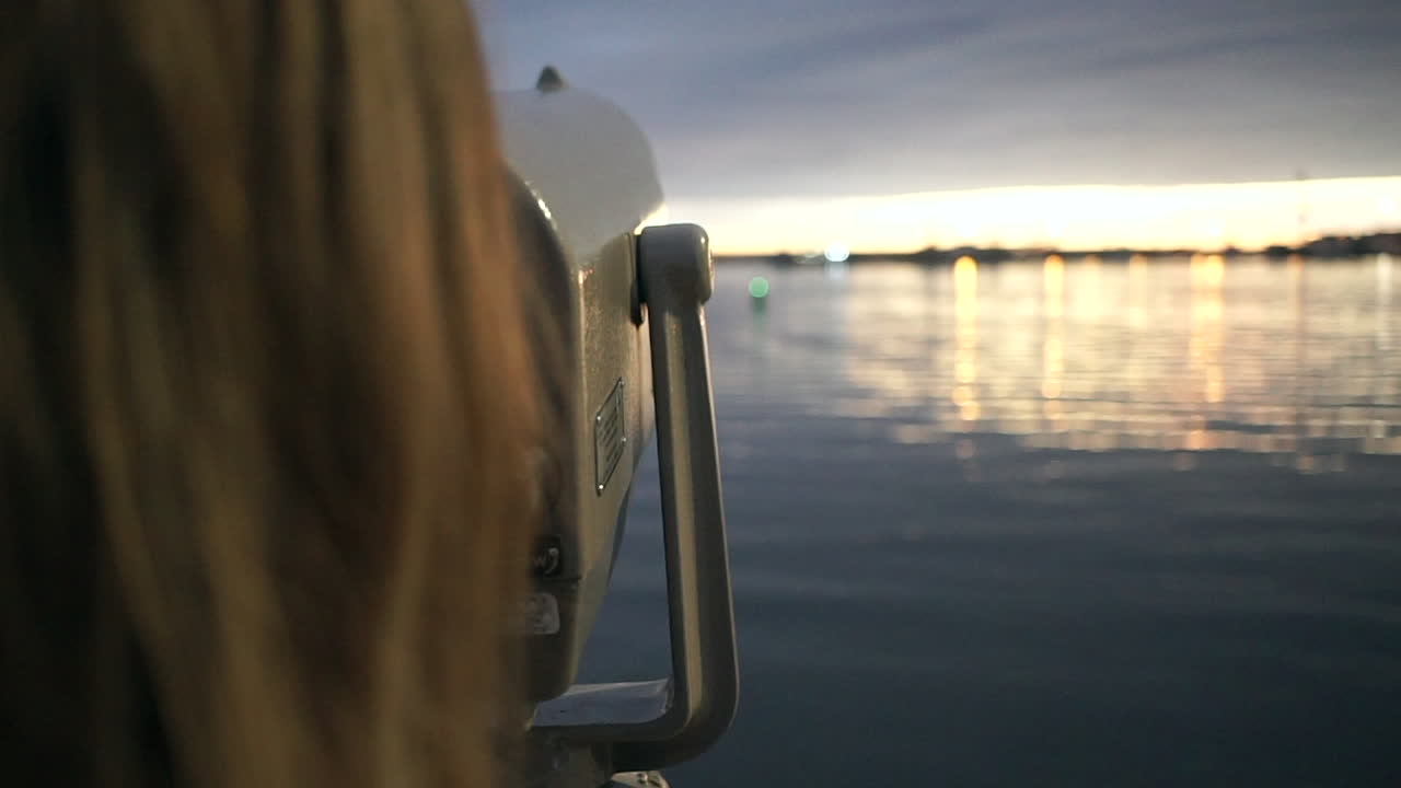 Woman looks through telescope and points at sunset