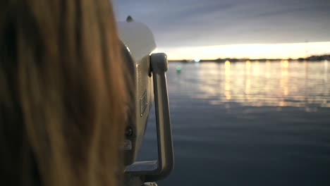 woman looks through telescope and points at sunset