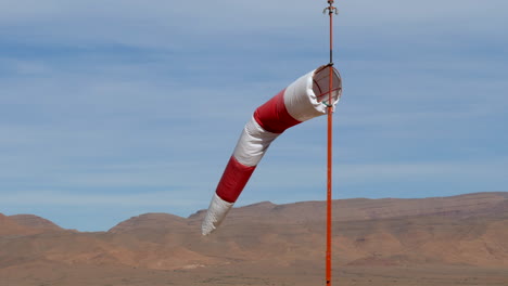 primer plano de una manga de viento aislada que sopla suavemente en el viento en un aeródromo del desierto, altas montañas en el fondo