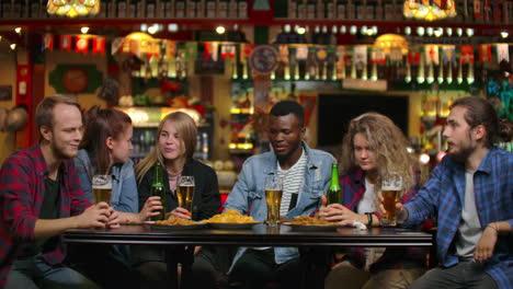 multi-ethnic group of young men and women drinking beer at a bar and having a fun discussion about the university.