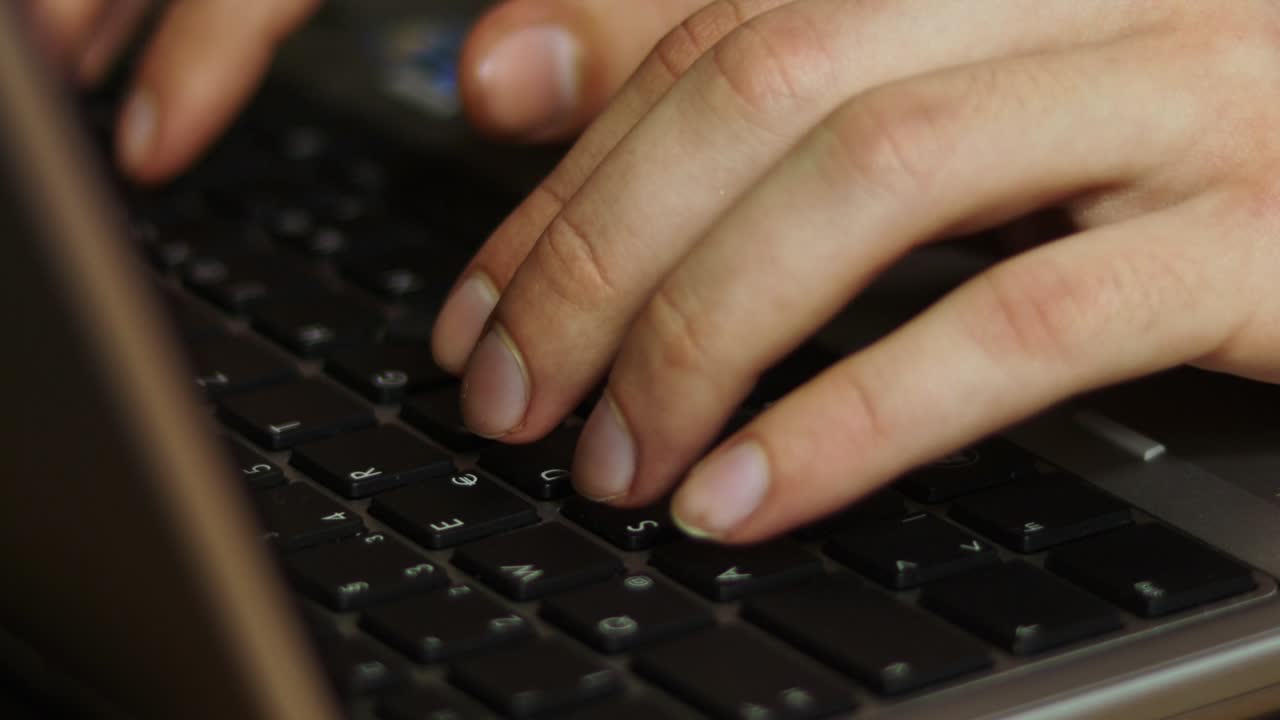 Close up of male hands typing on laptop keyboard side view.