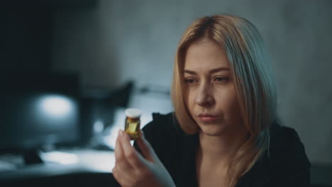 doubting lady with pill bottle thinks in semi-dark office