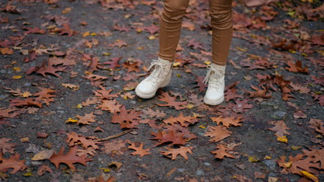 unrecognized woman stepping by the road covered with leaves. female legs in white boots having promenade in the autumn park.