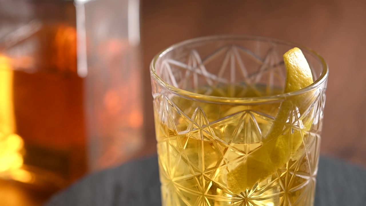Cocktail Rusty Nail in rotazione in un bicchiere old fashioned con ghiaccio, primo piano di una bevanda ambrata.