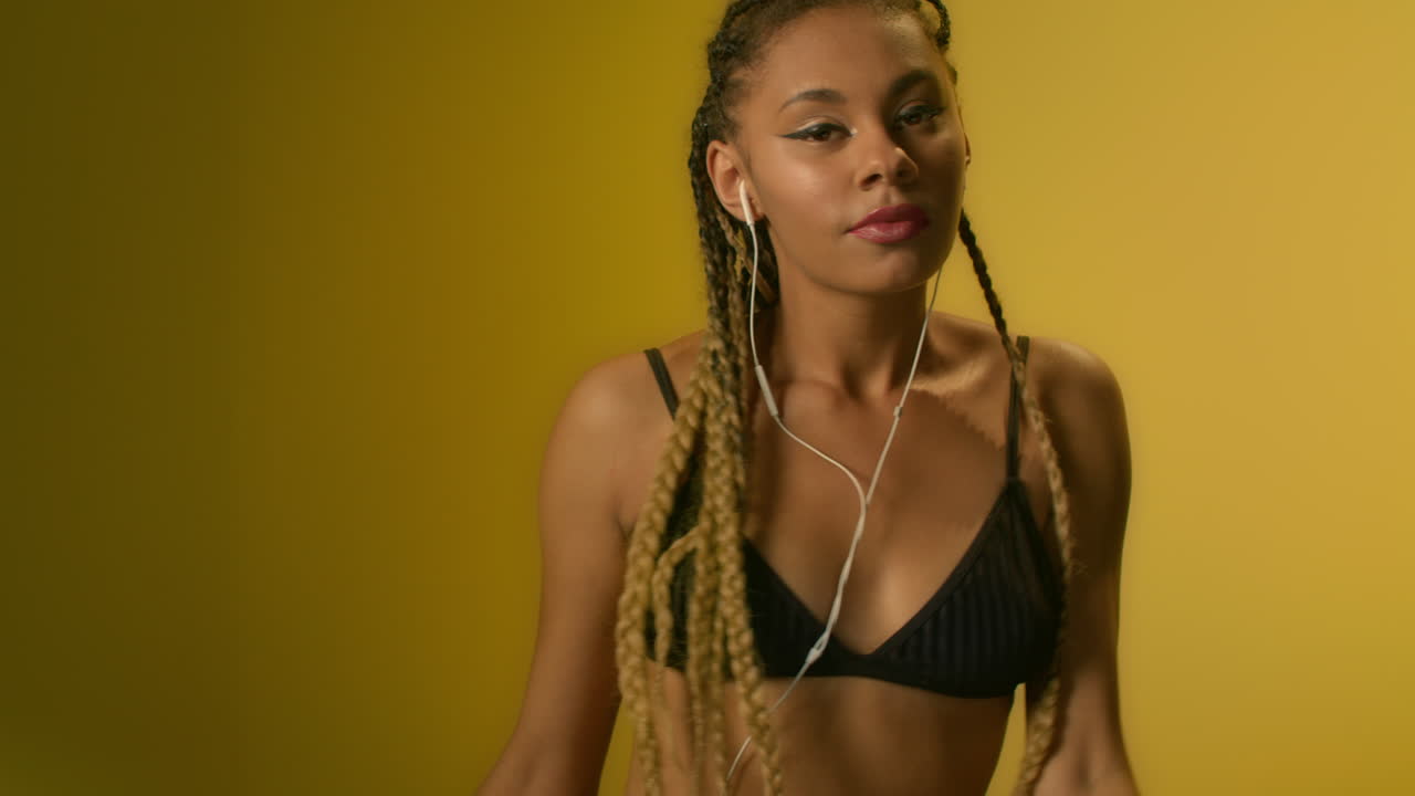 mujer bailando escuchando música en el teléfono móvil en auriculares sobre fondo amarillo