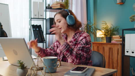 excited business woman listening music through wireless headphones sitting at home office desk