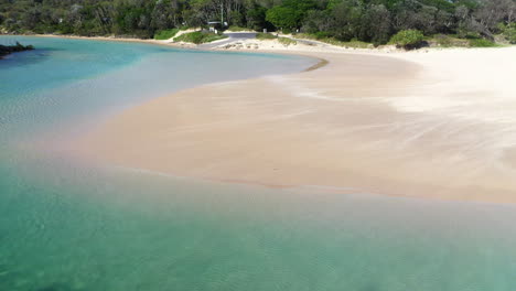 Wide-rotating-drone-shot-of-the-wind-blowing-sand-across-a-sand-bar-at-Hat-Head-New-South-Wales,-Australia