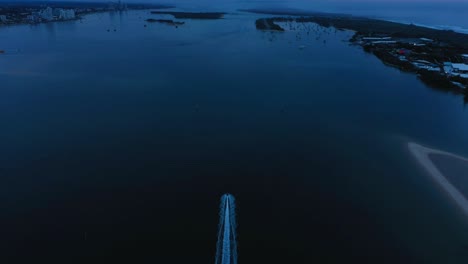 Lone-boat-heading-out-at-dawn-along-the-Gold-Coast-Broadwater,-drone-at-sunrise,-Australia