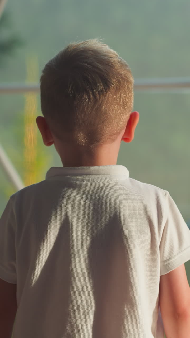 아이가 풍경을 바라보는 창문에 다가오고, 아이는 가에 팔을 고, 흐릿한 배경에서 느린 동작을 상상하고, 뒤쪽을 가까이 보고 있다.