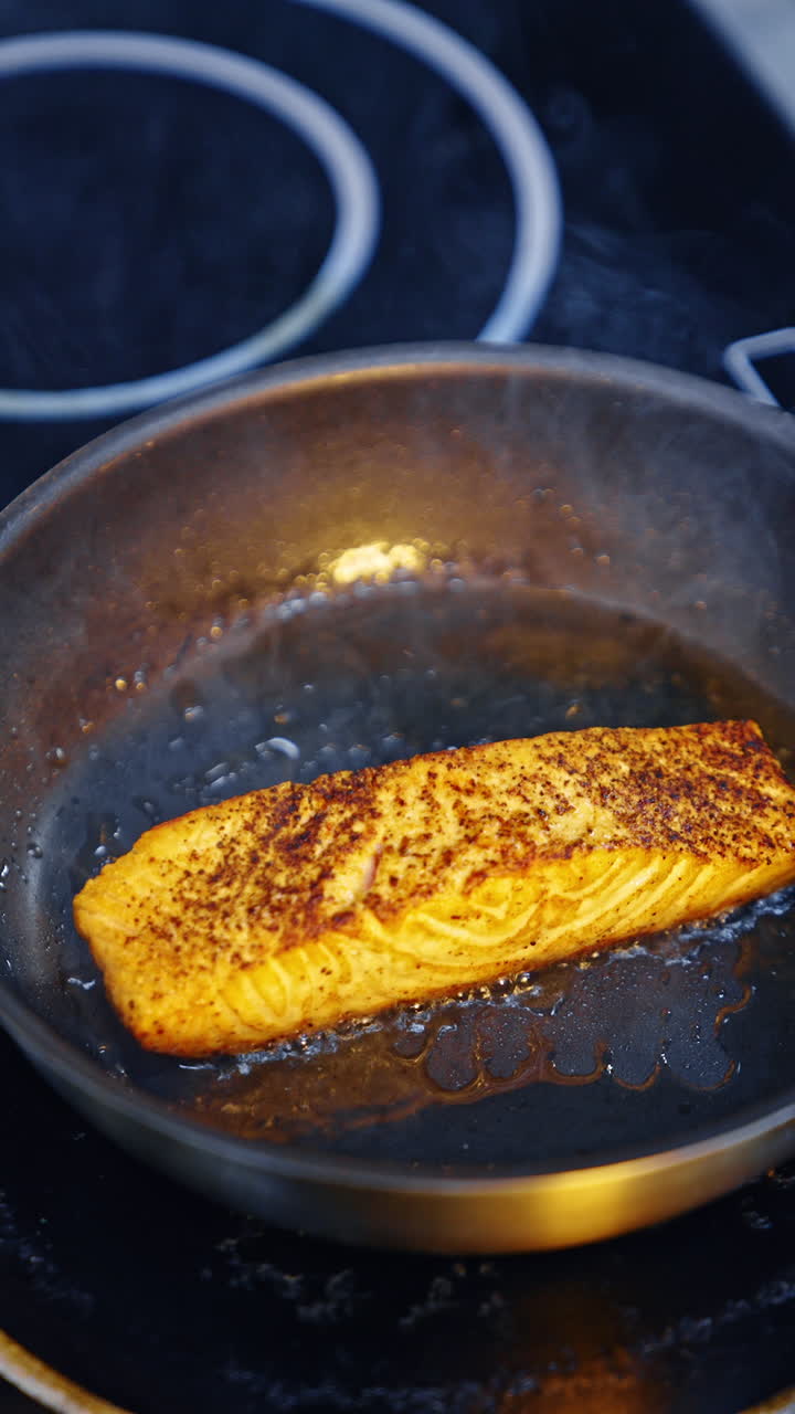 Cooking fish in the frying pan. Metal tongs are used to move the piece of fish. Close up. Vertical video.