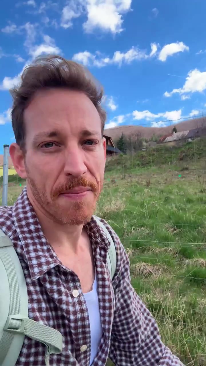 Reiseinnholdsskaper eller vlogger på tur utendørs med ryggsekk på en solrik sti på landet. Vertikalt UGC-opptak i selfie-stil. Mann snakker til kamera mens han går. Skogstur. Reel og story