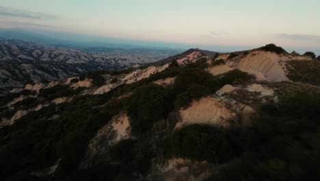 Fast-FPV-close-up-drone-shot-over-the-hilly-landscape-of-Calanchi-di-Aliano-in-Italy-during-sunset