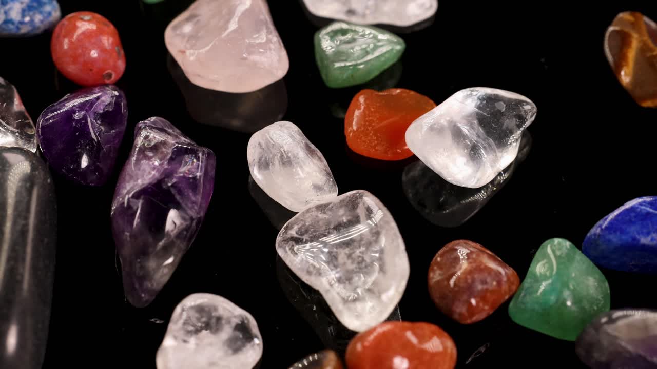 Colorful chakra stones arranged on a reflective black surface, highlighting their textures and hues under bright lighting