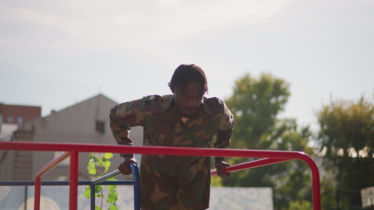 Black Soldier Standing On Red Play Structure At Sunrise, Camouflage Uniform Backlit By Warm Sun, Apartment Block Skyline, Quiet Contemplative Stance, Cinematic Silhouette And Reflective Mood