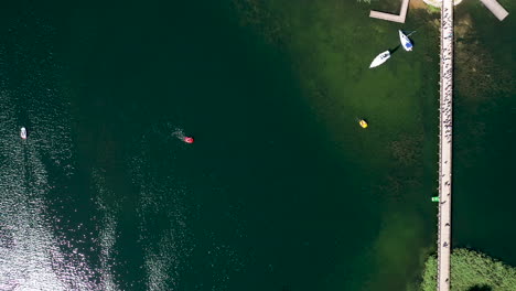 AERIAL:-Very-High-Altitude-Top-View-of-Trakai-Island-Bridge-with-Green-Color-Lake-and-Boats-Sailing-Around