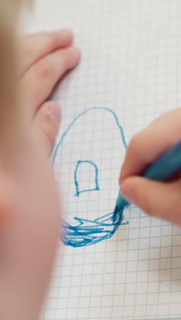 toddler boy colors donut with blue marker on copybook page at table closeup. little pupil draws picture at art lesson in preschool classroom upper view