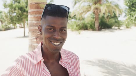 Retrato-De-Un-Hombre-Afroamericano-Feliz-Tocando-La-Guitarra-Y-Cantando-En-Una-Playa-Soleada,-Cámara-Lenta