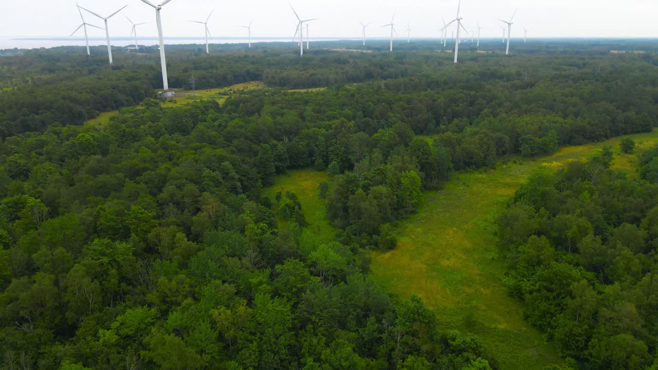 Aerial drone revealing wide shot of white colored wind turbines on a cloudy and foggy peninsula at Paldiski spinning and rotating in the wind while blue Baltic sea is in the background horizon