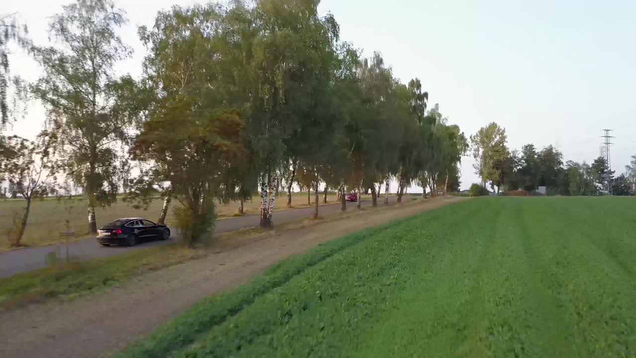 A drone shot of an electromobile driving besides the tree road