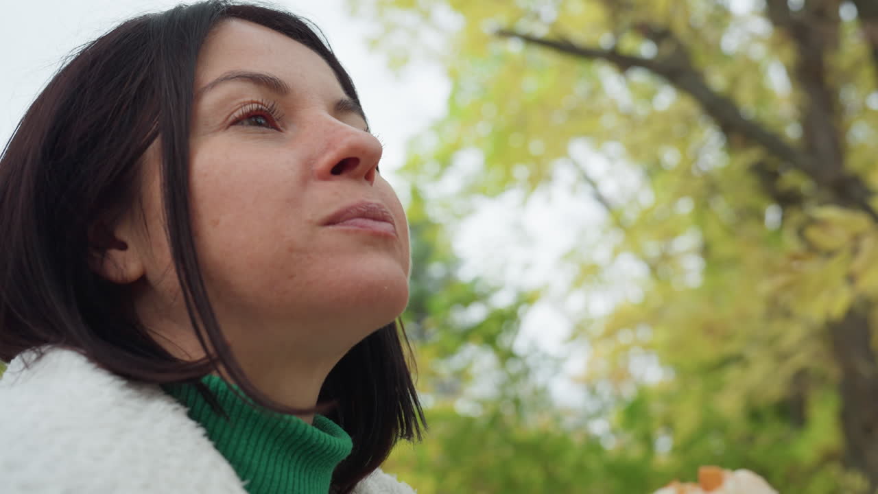 Ritratto di donna bianca in un parco autunnale, musicista rock contemplativo con giacca di pelle e dolcevita verde, primo piano di profilo con bokeh morbido di foglie gialle, aria fresca e frizzante, sguardo pensieroso