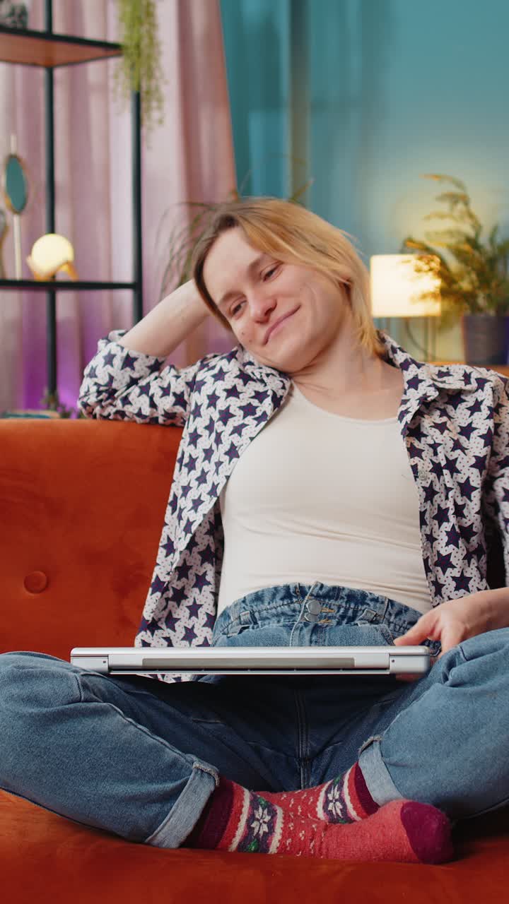 Glad, ung og avslappet kvinne sitter på sofaen og lukker laptopen etter endt arbeidsdag i stuen.