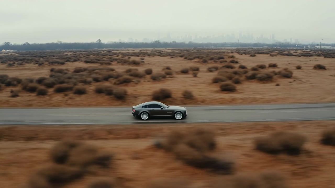 Coupé argentata che guida su strada nel deserto, ripresa aerea panoramica di veicolo elegante che sfreccia oltre arbusti sparsi.