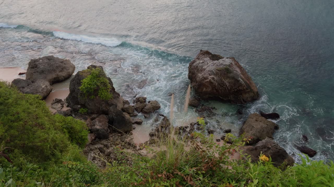 Spectacular aerial view captures the rugged beauty of Bingin Beach, Bali. Waves crashing against rocks, lush greenery, and serene waters reflect a breathtaking coastal landscape
