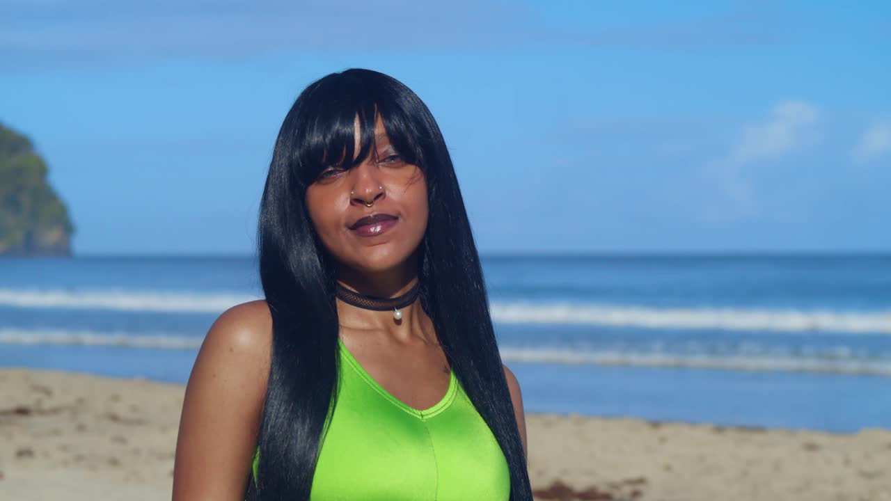 Una chica con un elegante bikini verde bosque y negro se para en la orilla, con el agua caribeña brillante arremolinándose alrededor de sus tobillos.