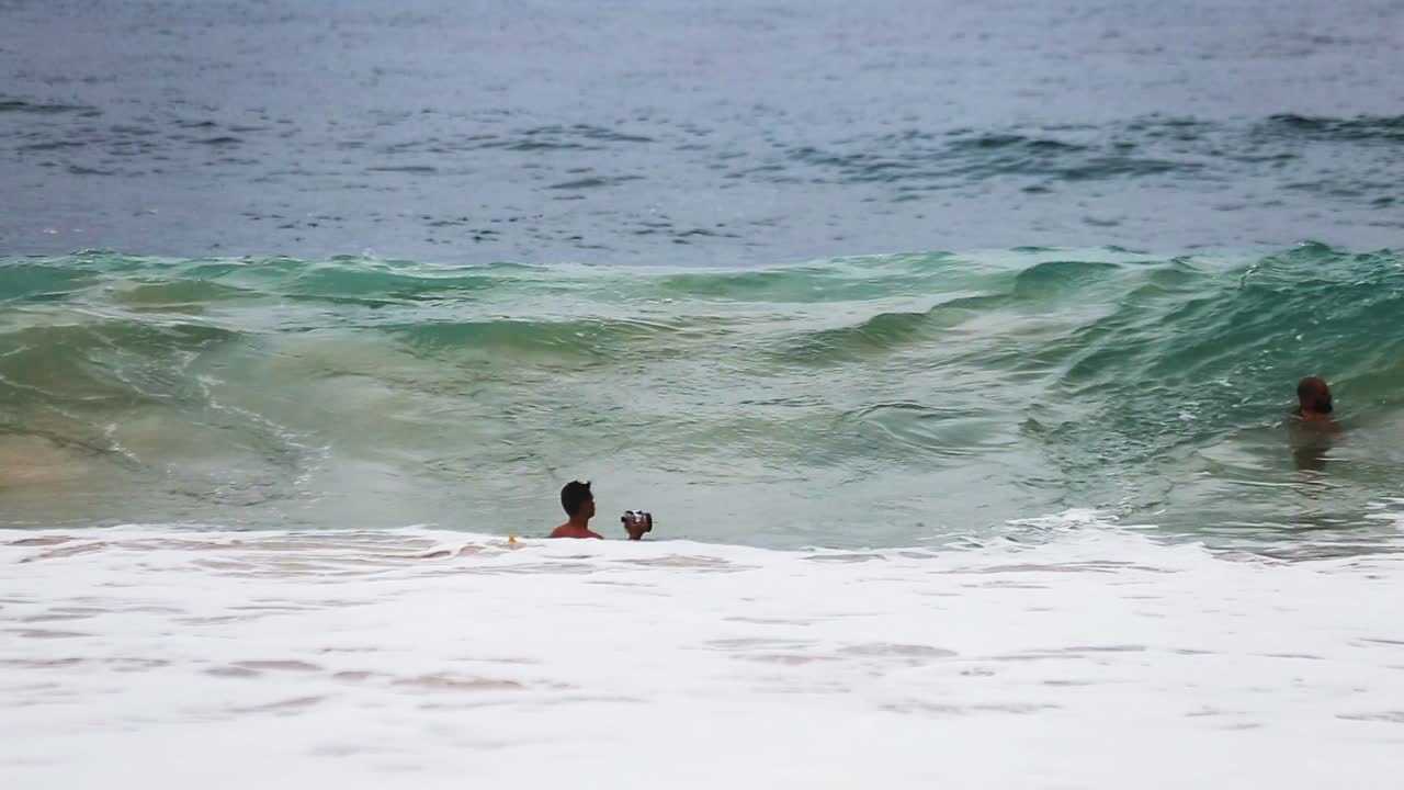 en la perspectiva de la costa de un hombre en el agua tratando de tomar fotografías de las olas en la playa de arena, oahu, hawaii con lavado blanco de la ola anterior corriendo por la playa