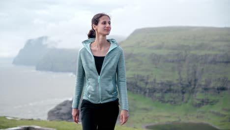 a woman walking near leitisvatn, faroe islands, surrounded by cliffs and nature