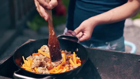 cu young man standing near the brazier mixes pork and carrots with onion wooden spatula