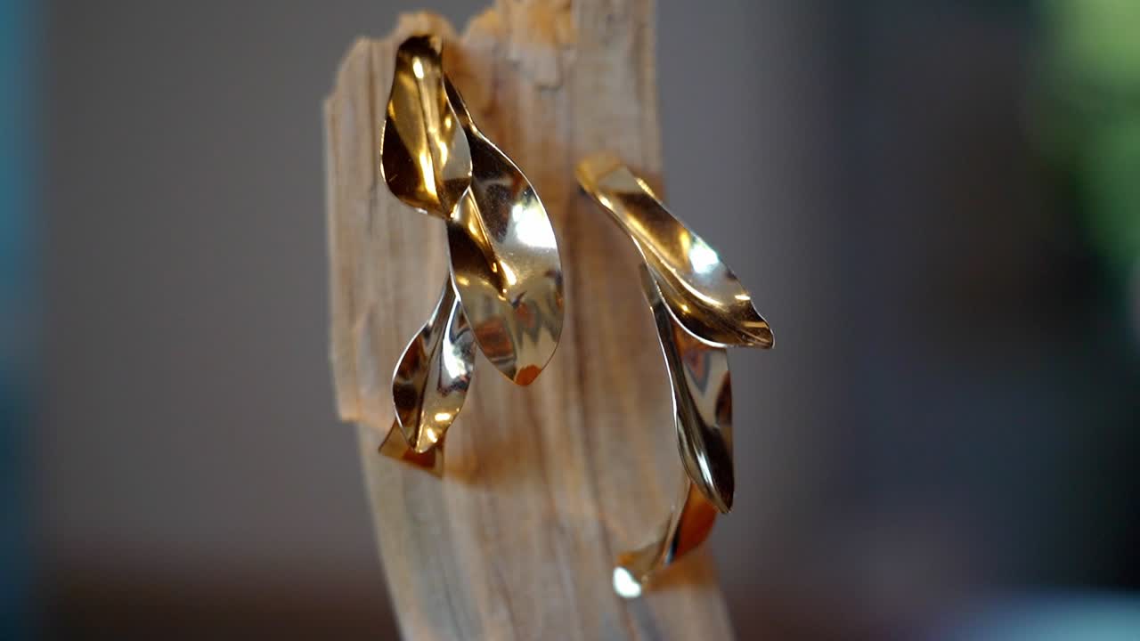 Close-up of abstract gold earrings on a wooden display
