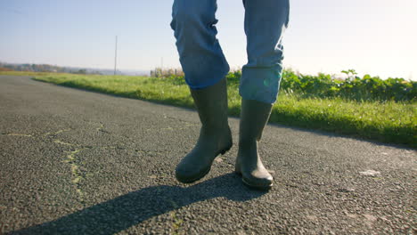 usando vaqueros mientras camina con botas industriales en el asfalto hacia la hierba a la orilla de la carretera, disparo de seguimiento de bajo ángulo