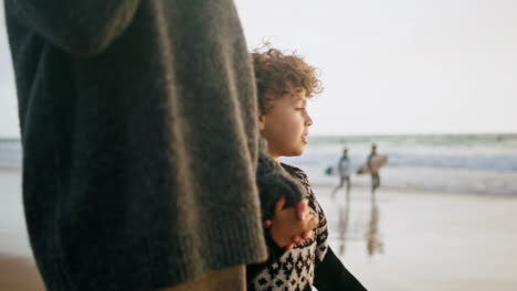 cute boy walking coast holding mother hand. smiling child talking unknown parent