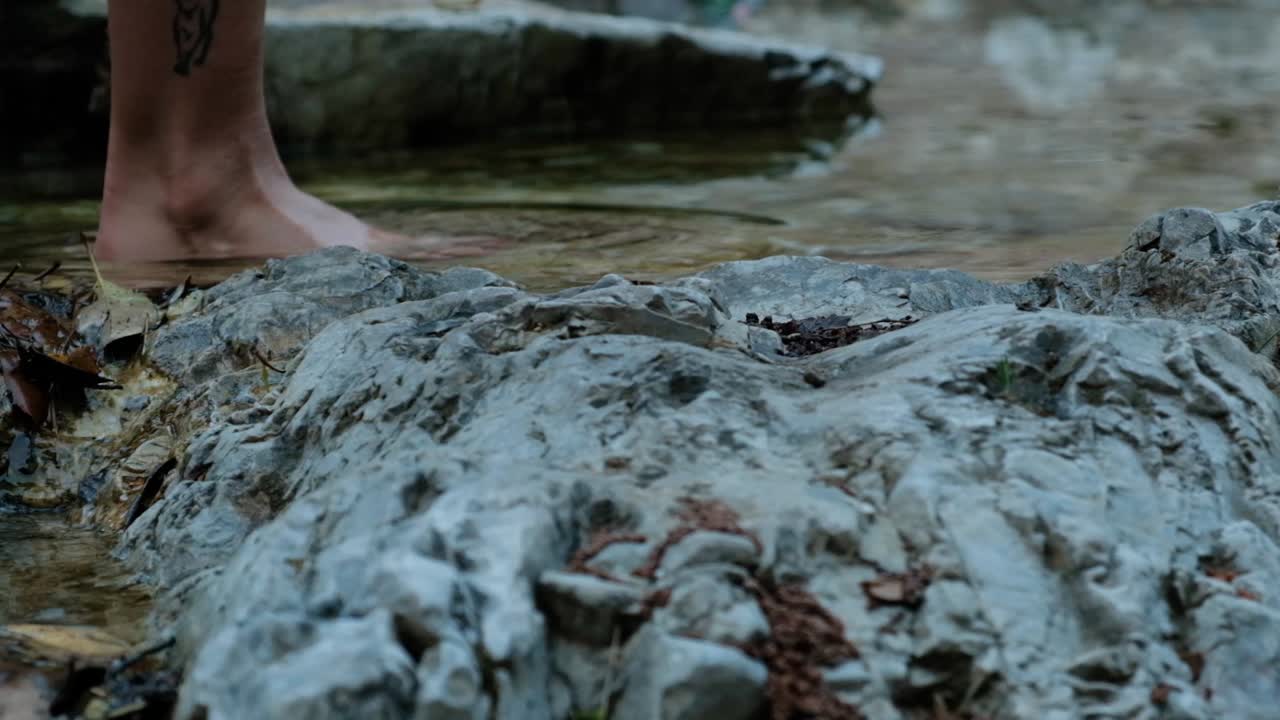 여자는 바위가 많은 개울에서 맨발로 걷는다