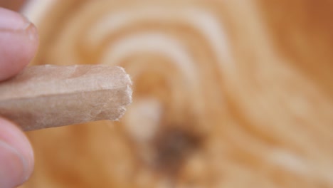 close-up of a hand holding a broken paper coffee stirrer, with latte art in the background