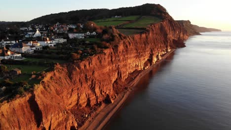 aerial forward shot of the red jurassic cliffs at sidmouth south west england at sunrise bathed in golden sunlight