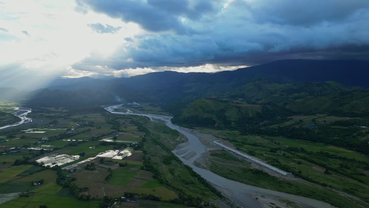 Panorama Sungai Chico yang luas menampilkan saluran yang terjalin, pegunungan yang teduh, dan berkas sinar matahari yang menembus tutupan awan Bontoc, Nueva Vizcaya, Filipina