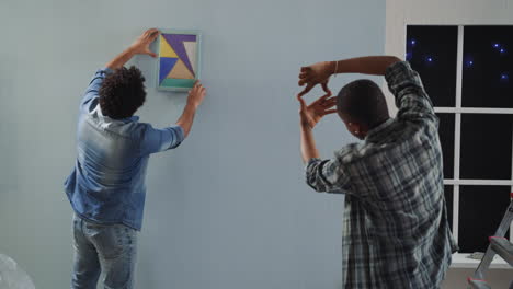 Black-man-chooses-place-to-hang-picture-on-wall-with-friend