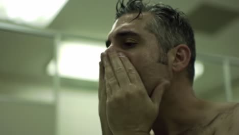 a man's reflection: battling emotions in the mirror while water drips down his face, a moment of vulnerability and self-reflection captured in a private space